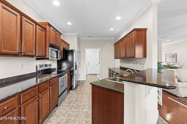 kitchen featuring a sink, a kitchen breakfast bar, ornamental molding, appliances with stainless steel finishes, and dark stone countertops