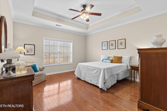 bedroom featuring hardwood / wood-style flooring, visible vents, and a tray ceiling