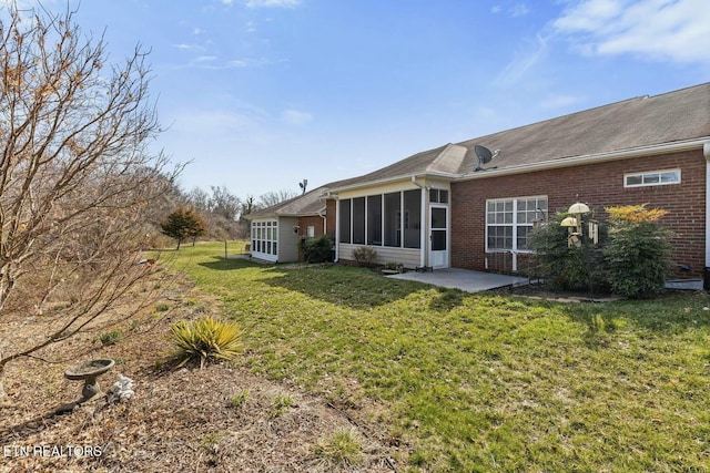 back of property with a yard, brick siding, a patio area, and a sunroom