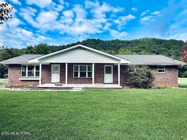 ranch-style house with covered porch, brick siding, a front yard, and a shingled roof