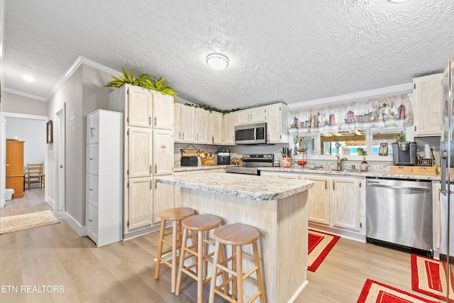 kitchen with appliances with stainless steel finishes, ornamental molding, a sink, light wood-type flooring, and a kitchen breakfast bar