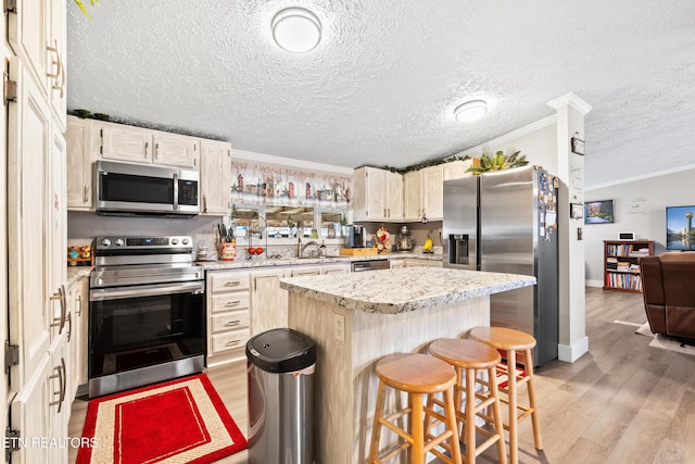 kitchen featuring light wood-style flooring, stainless steel appliances, a breakfast bar, a sink, and ornamental molding