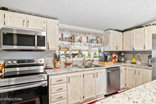 kitchen with ornamental molding, light stone countertops, stainless steel appliances, a textured ceiling, and a sink