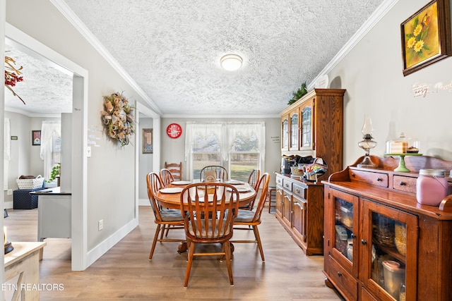 dining space featuring light wood-style flooring, a textured ceiling, ornamental molding, and baseboards