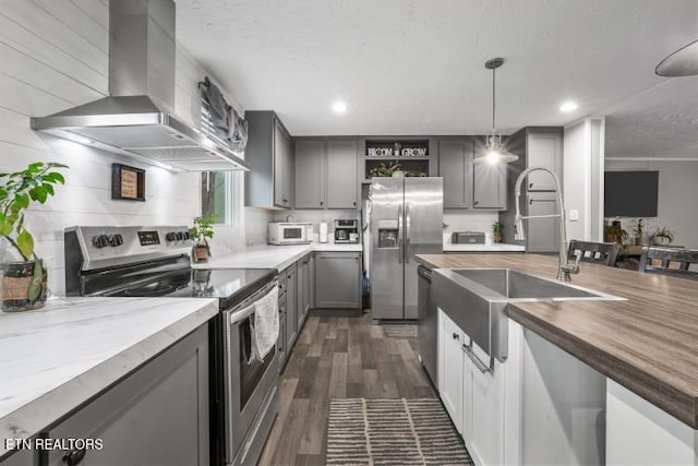 kitchen with wall chimney exhaust hood, appliances with stainless steel finishes, gray cabinets, open shelves, and a sink