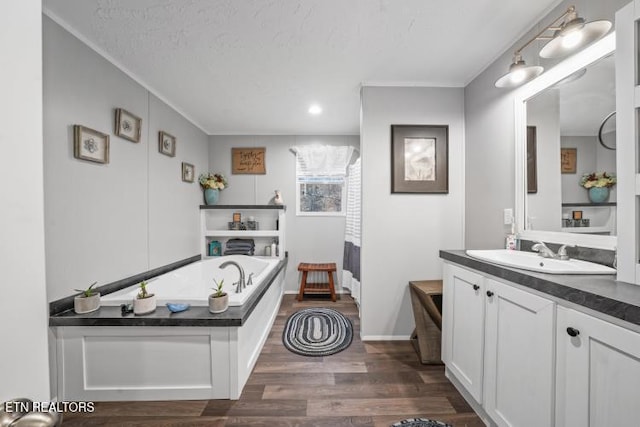 bathroom featuring a garden tub, a textured ceiling, vanity, wood finished floors, and baseboards