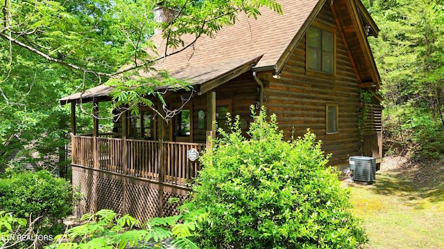 view of side of property with a shingled roof, a chimney, log siding, a wooden deck, and central AC