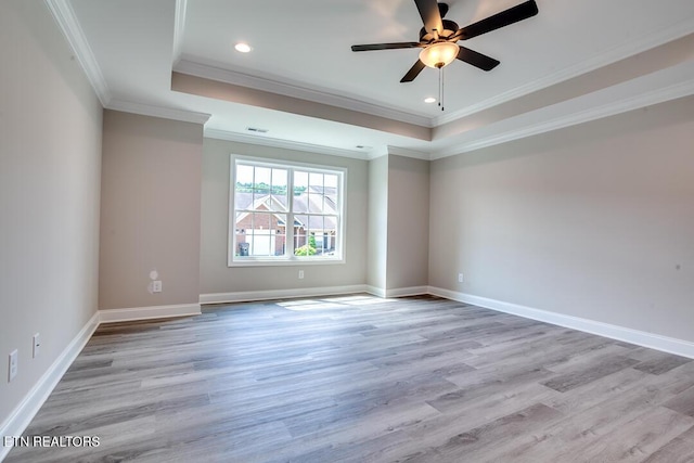 empty room with light wood finished floors, baseboards, a tray ceiling, and ornamental molding