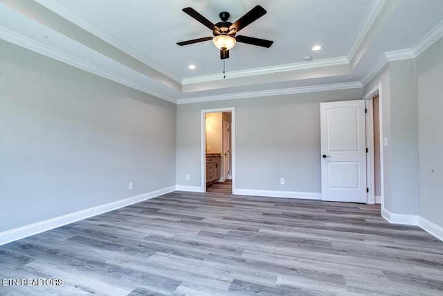 unfurnished bedroom with ornamental molding, a raised ceiling, baseboards, and wood finished floors