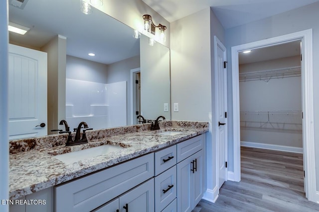 bathroom with wood finished floors, a sink, baseboards, and double vanity