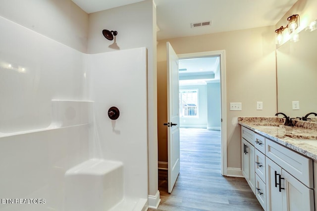 full bathroom with double vanity, baseboards, visible vents, wood finished floors, and a sink