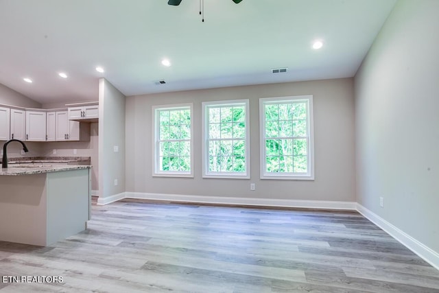 kitchen with light wood-style flooring, visible vents, white cabinetry, and light stone counters