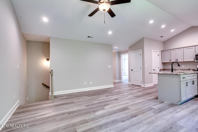 kitchen featuring a center island with sink, visible vents, vaulted ceiling, light stone countertops, and light wood-type flooring