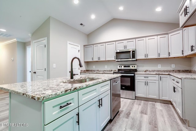 kitchen with light stone counters, a sink, light wood-style floors, appliances with stainless steel finishes, and an island with sink