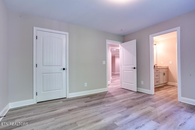 unfurnished bedroom with light wood-style floors, a closet, baseboards, and ensuite bathroom