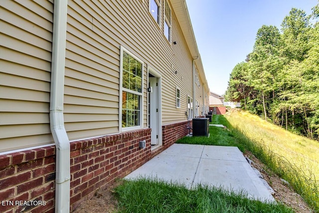 view of side of property featuring cooling unit, a patio area, and brick siding