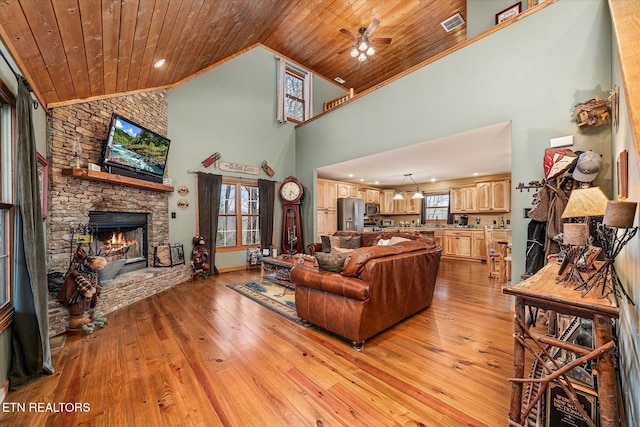 living area with light wood-type flooring, a stone fireplace, wooden ceiling, and high vaulted ceiling