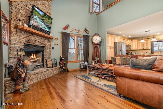 living room with light wood finished floors, a high ceiling, baseboards, and a stone fireplace