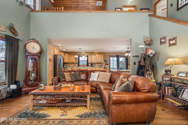 living area with light wood-type flooring, a high ceiling, and visible vents