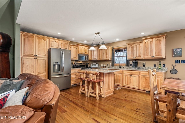 kitchen featuring light brown cabinets, stainless steel appliances, open floor plan, hanging light fixtures, and a center island