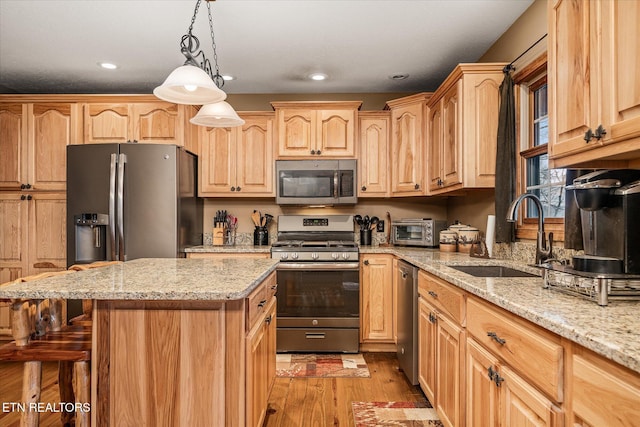 kitchen featuring a kitchen island, a sink, appliances with stainless steel finishes, light stone countertops, and decorative light fixtures