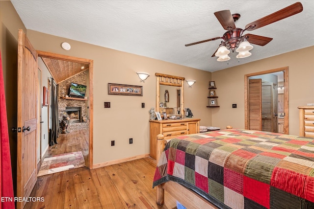 bedroom with a textured ceiling, a large fireplace, baseboards, vaulted ceiling, and light wood-type flooring