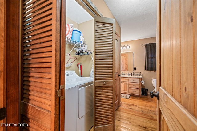 clothes washing area with light wood-type flooring, laundry area, a textured ceiling, and separate washer and dryer