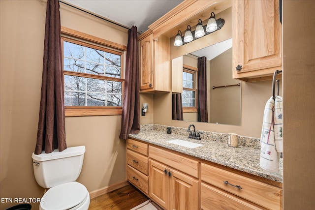 half bath with toilet, baseboards, wood finished floors, and vanity