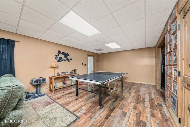 recreation room with a paneled ceiling, baseboards, and wood finished floors