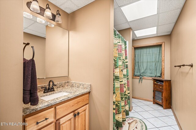 full bathroom with tile patterned flooring, vanity, a paneled ceiling, and baseboards