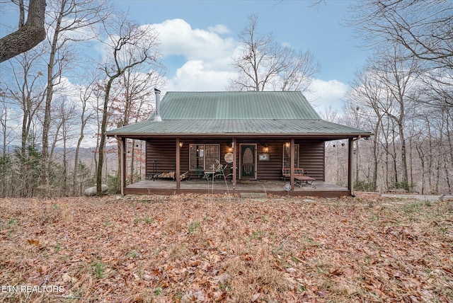 chalet / cabin featuring metal roof, a chimney, a porch, and log veneer siding