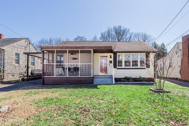 view of front of property featuring entry steps, a sunroom, roof with shingles, and a front lawn