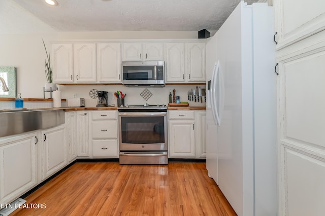 kitchen with stainless steel appliances, a textured ceiling, light wood-style floors, white cabinetry, and a sink