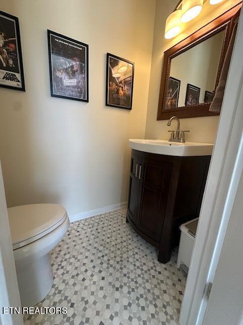 half bathroom with toilet, tile patterned floors, baseboards, and vanity