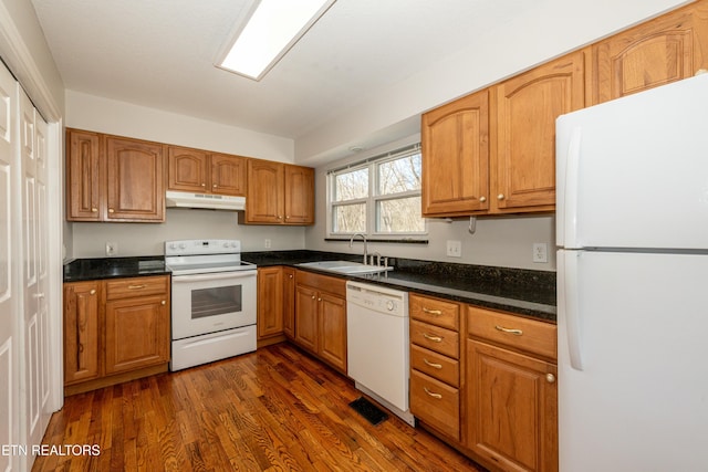 kitchen with white appliances, dark countertops, dark wood-style flooring, under cabinet range hood, and a sink