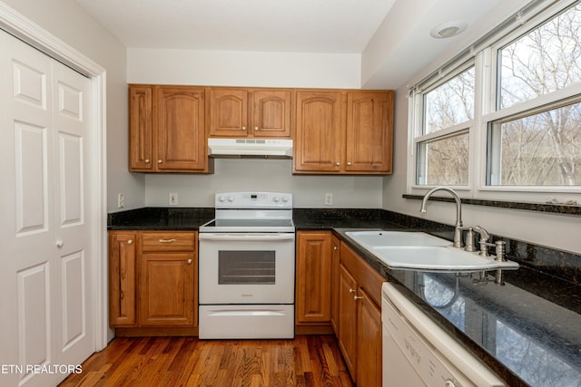 kitchen with under cabinet range hood, white appliances, dark wood-type flooring, a sink, and brown cabinets