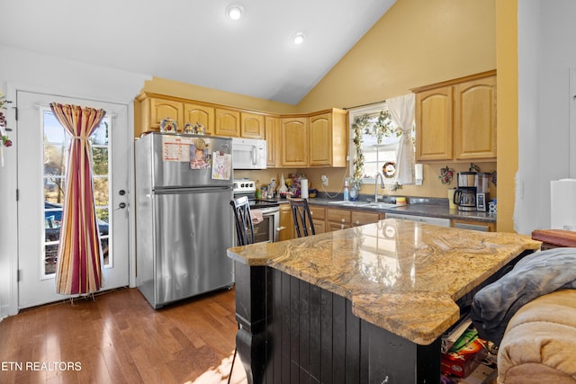 kitchen with lofted ceiling, wood finished floors, stainless steel appliances, light brown cabinets, and a sink