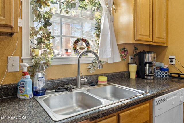 kitchen with a textured wall, dark countertops, a sink, and dishwasher