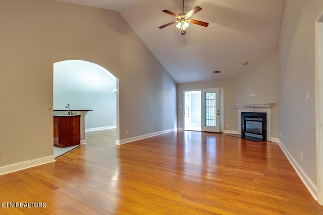 unfurnished living room with high vaulted ceiling, a fireplace with flush hearth, a ceiling fan, baseboards, and light wood-style floors