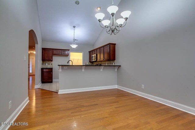 kitchen featuring a breakfast bar, decorative light fixtures, stainless steel microwave, and a peninsula