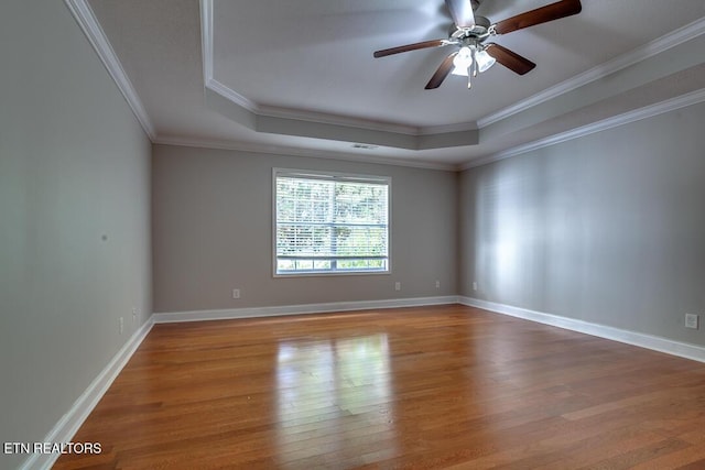 spare room with a tray ceiling, crown molding, baseboards, and wood finished floors