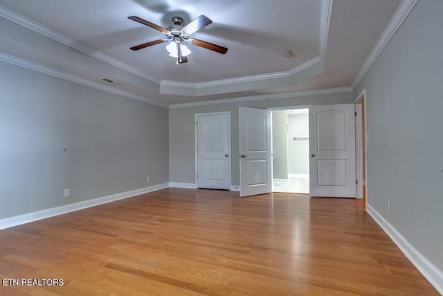 unfurnished bedroom with light wood-type flooring, baseboards, visible vents, and a tray ceiling