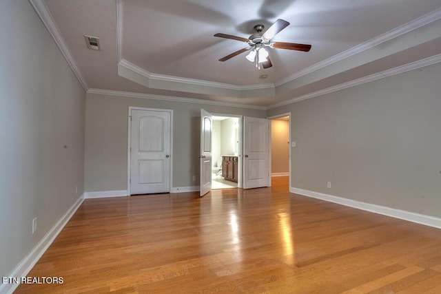 unfurnished bedroom with visible vents, baseboards, a raised ceiling, crown molding, and light wood-style floors