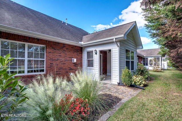 doorway to property with roof with shingles, a lawn, and brick siding