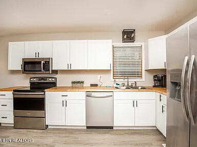 kitchen with light wood finished floors, butcher block counters, appliances with stainless steel finishes, white cabinetry, and a sink