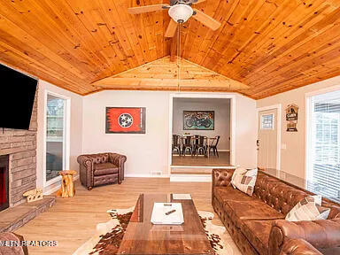 living room featuring wood ceiling, vaulted ceiling, a stone fireplace, and wood finished floors