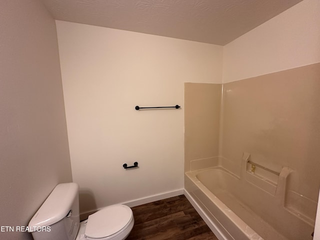 bathroom with a textured ceiling, toilet, wood finished floors, baseboards, and a tub