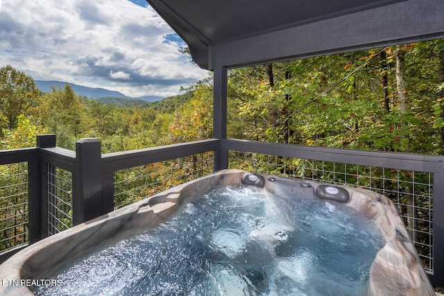 exterior space featuring a hot tub, a mountain view, and a view of trees