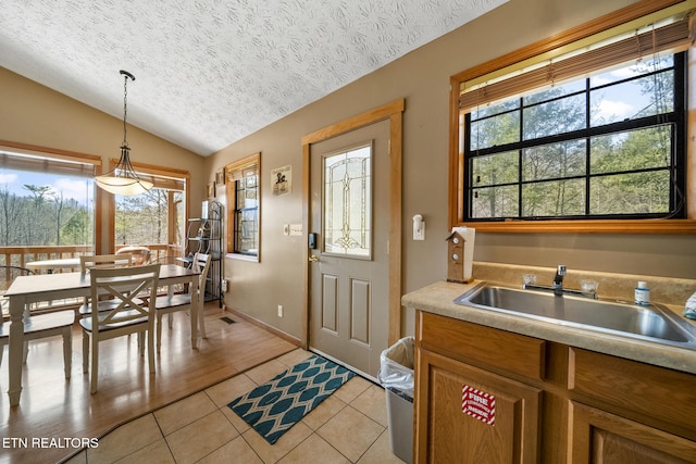 kitchen with light tile patterned floors, a textured ceiling, a sink, vaulted ceiling, and hanging light fixtures