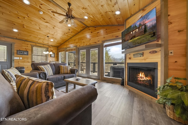 living area featuring lofted ceiling, wooden ceiling, wood walls, wood finished floors, and a glass covered fireplace